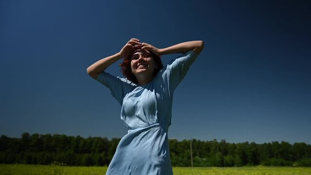 Caucasian young woman in a blue dress enjoys a breath of wind in a field. Video 360 degrees. 
