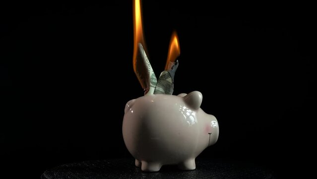 Burning home bank on black background. A view of dollars in fire in piggy bank. A concept of finance crisis in the world.