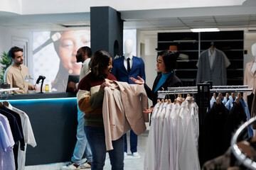 Smiling african american woman holding jacket on hanger and talking with consultant in boutique....