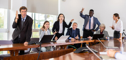 Multiracial group of age-diverse business people in formalwear having an emotional dispute and verbal altercation during corporate group meeting in conference room at office finding no compromise in