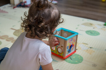 Infant baby playing with colorful shape sorter box toy on a playmat. Toddler boy playing with toys at nursery, daycare or kindergarten while sitting. A child with educational toys, Early development.