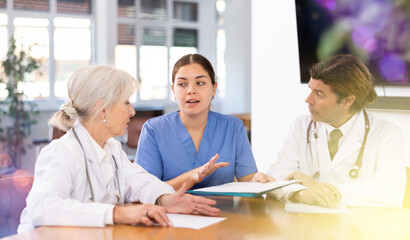 Adult man, elderly woman and young woman doctors having discussion at table