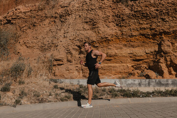 Athletic young man in sports clothing running against rocky mountain outdoors