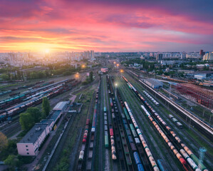 Fototapeta na wymiar Aerial view of freight trains at colorful sunset. Railway cargo wagons on railroad. Top view of wagons, city, pink sky with clouds at night. Depot of freight trains. Railway station. Transportation