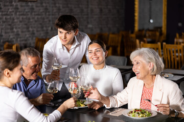 In cozy restaurant, elderly family and adult daughters with husband enjoy festive lunch,...