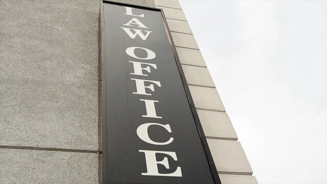 law office sign in white capital letter on black background on side of building vertically with sky in background