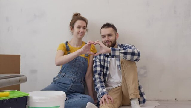 Happy family couple making hand heart looking on each other during apartment redecoration. Renovation and improvement new home. slow motion. Family relationship concept. 