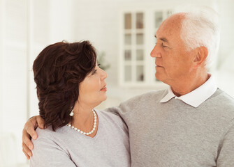 Portrait of cute happy Caucasian couple of retired husband and wife hugging indoors.