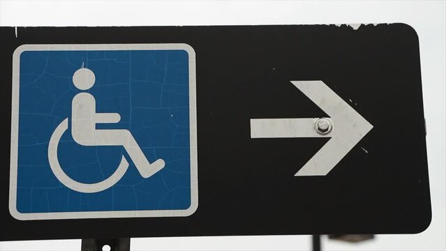 handicap sign blue logo with white arrow on its right pointing right on black rectangle horizontal sign on post with sky in background, space on right