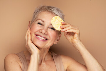 Photo of nice old woman use sponge remove make up on beige background