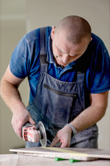 Professional tiler cutting tile with angle grinder. Construction, renovation, repair apartment.