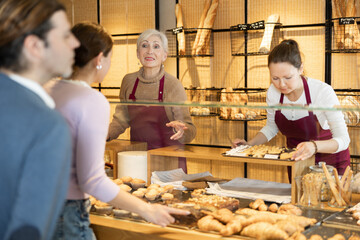 Two smiling friendly female bakers in maroon aprons working behind counter in small family...