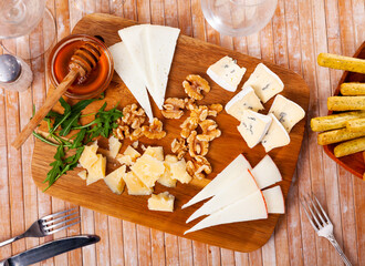 Cheese board served with honey and walnuts and decorated with herb on wooden table.