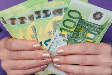 One hundred euro banknotes in female hands in a purple hoodie.Income of women in European...