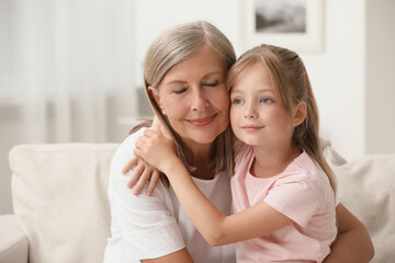 Happy grandmother hugging her granddaughter at home, space for text