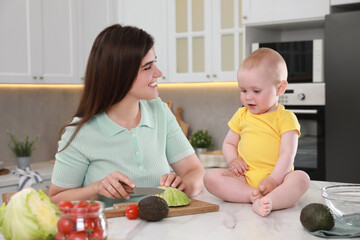 Naklejka premium Happy young woman with her cute baby spending time together in kitchen
