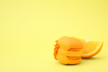 Delicious macaron and orange slice on yellow background, closeup. Space for text