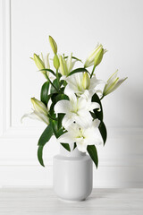 Fototapeta na wymiar Beautiful bouquet of lily flowers in vase on light table near white wall