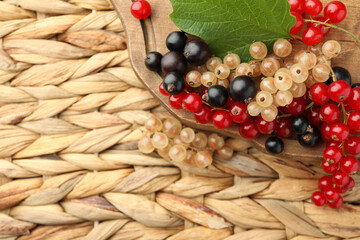 Different fresh ripe currants and green leaf on wicker surface, flat lay. Space for text