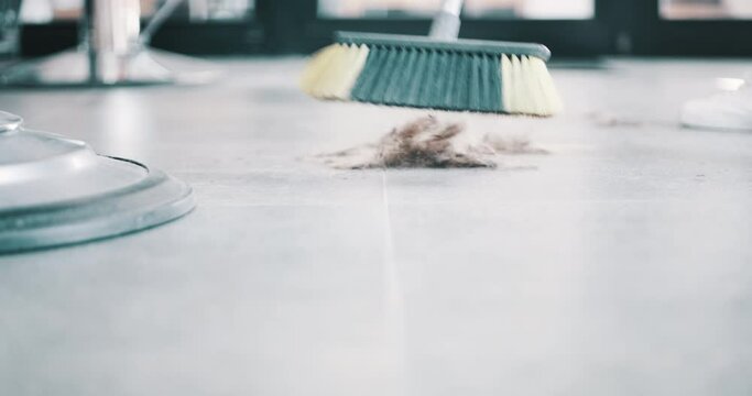 Cleaning, sweeping hair and broom in a barbershop for dirt, salon or cleanliness. Sweep floor, closeup and tools to clean the ground of a haircare business, chores and tidying up after service
