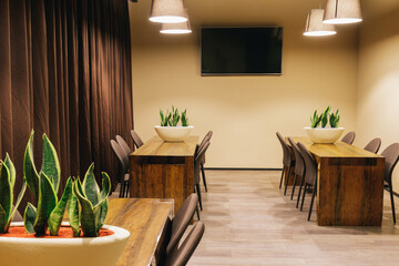 View of the room interior with a wood tables, chairs, brown curtains and tv screen.
