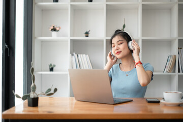 Pretty young woman listening to music with laptop computer and relaxing while sitting on chair at home.