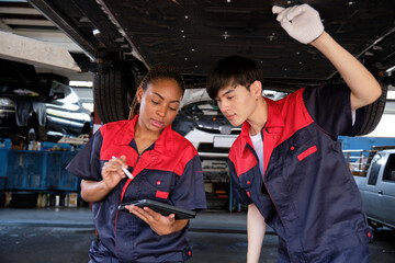 Two professional automotive worker partners discuss mechanical check undercarriage of lifted...