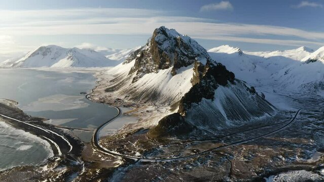 Aerial tilt shot of a winding road and snowy mountains, sunny winter evening in south Iceland