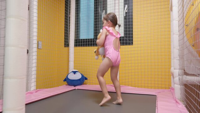 Smiling cheerful toddler girl jumping on trampoline at indoor playground - Slow motion