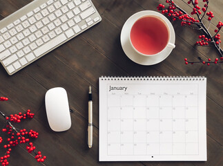 Top down view of office desk with computer keyboard, cup of tea and calendar with a month of January