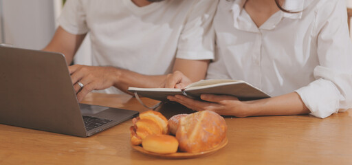 Handsome man sitting near his wife at kitchen. Family couple see social media, surf the web while sitting at kitchen table with generic laptop. Couple working with laptop at home