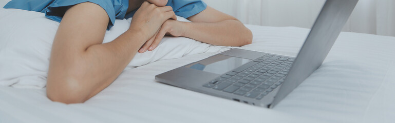 Young Asian woman with beautiful face, long hair, blue shirt lying on bed in white bedroom at home with cup of coffee and video call with laptop talking to relatives on vacation. holiday concept.