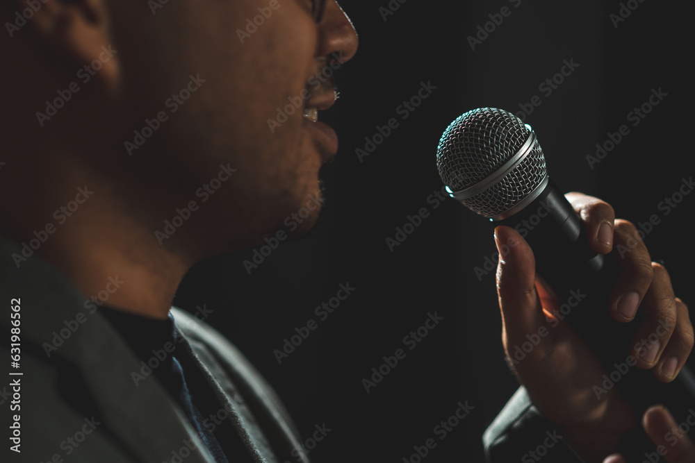 Canvas Prints Confident successful speaker man talking on stage with spotlight strike through the darkness at corporate business event. Public speaker giving talk at conference hall. Stand up comedian.