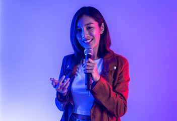 Attractive singer woman singing music on stage with spotlight strike through the darkness at concert event. Musician performing live with neon light in hall.