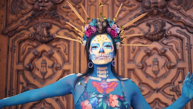 Dancer in costume for dia de los Muertos, woman with long dark hair in traditional costume and Mexico Catrina makeup standing near wooden ornamental door and holding skirt. Day of death.
