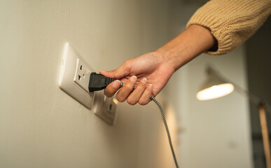 Close up woman hand put on or remove Electric plug cable in socket. Electrical equipment wires and power strips on the wall. Earth Hour saving  energy.