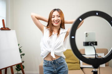 Young trendy influencer asian woman dancing on mobile phone at home in living room. Creator vlogger...