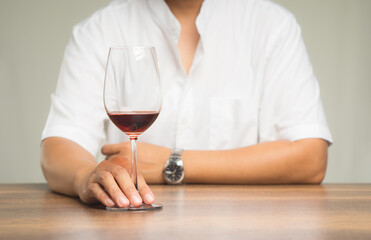 Businessman's right hand touches the base of a glass of red wine while sitting at the table