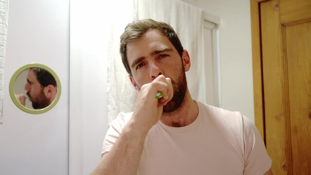 close up fornt view of a young man brushing teeth looking at camera, handsome guy enjoying morning oral hygienic routine, beauty male care