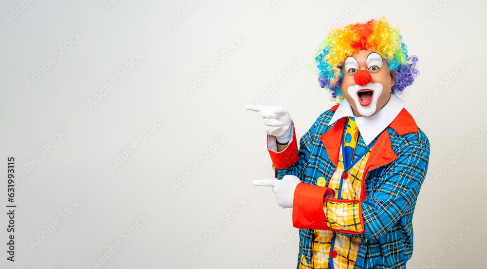 Wall mural mr clown. portrait of funny comedian face clown man in colorful uniform pointing finger to copy spac