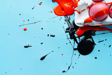 Close-up shot of blue surface with black and orange paint drops, white carton with bright pink eggs standing on it  
