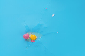 Raw egg yolk against turquoise background, its shell covered with bright pink paint lying next to it