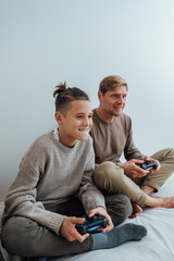 Teenager boy having fun enjoying play console video game with father while sitting on bed at home.