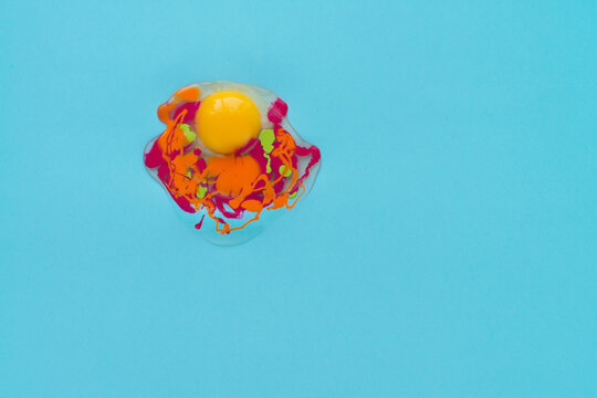 Unusual approach to raw egg representation: egg white and yolk with addition of orange, lime and fuchsia paints against turquoise background
