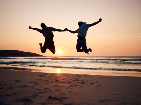 Beach, sunset and silhouette of couple jump, holding hands and enjoy fun quality time together on summer holiday. Energy, ocean sea and excited man, woman or people celebrate Australia vacation