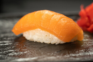 Japanese cuisine. Salmon sushi nigiri with reflection on dark stone background.