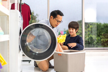 Family asian father and kid little boy son having fun doing household chores doing laundry dirty clothes into the washing machine together in laundry room at home