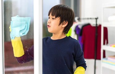 Kid little asian boy son having fun doing household cleaning and washing in protective gloves using...