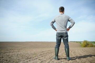 A farmer in boots works in a field sown in spring. An agronomist walks the earth, assessing a plowed field in autumn. Agriculture.