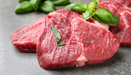 Cut fresh beef meat with basil leaves on grey table, closeup